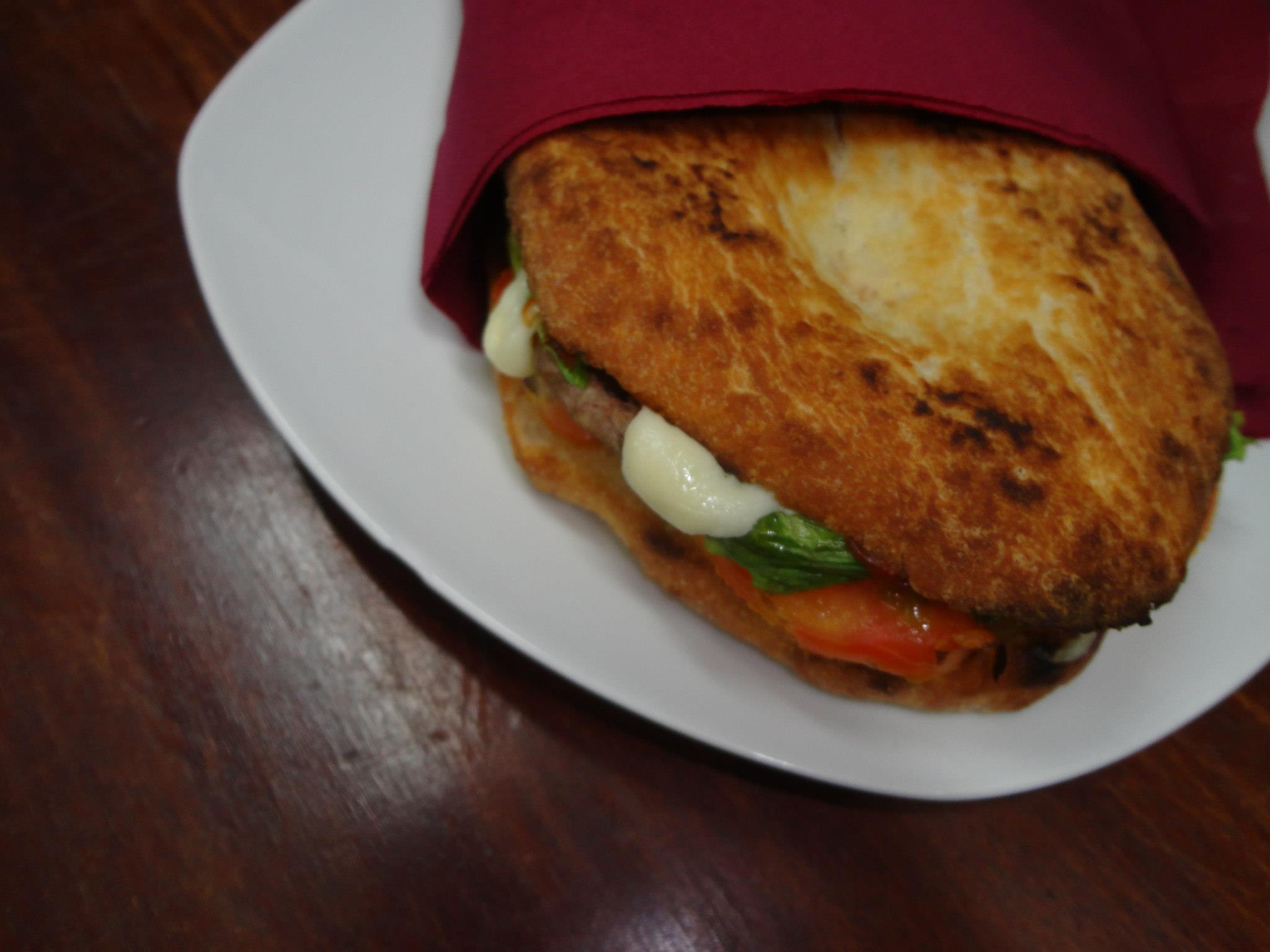 Panino Il Quartino in impasto pizza dorato con hamburger, pomodoro, lattuga e salsa bianca, tovagliolo bordeaux su piatto bianco