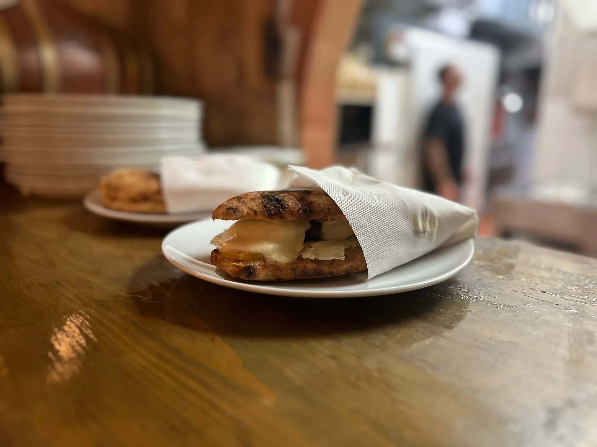Panino di pasta da pizza bruciacchiata farcito con formaggio fuso, avvolto in un tovagliolo su piatto bianco, de Il Quartino