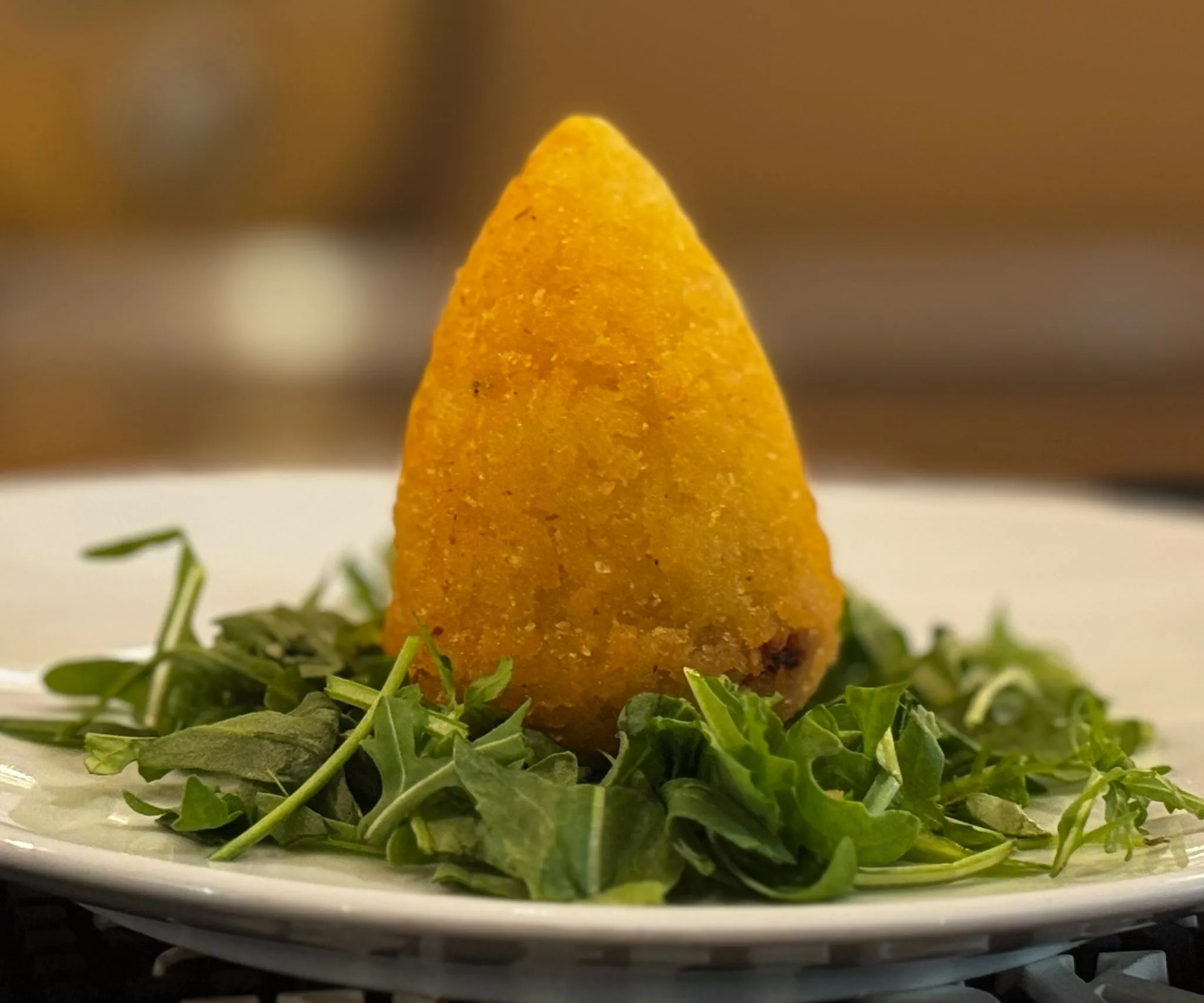 Arancino a punta dorato e croccante su letto di rucola fresca in un piatto bianco, fritto artigianale de Il Quartino
