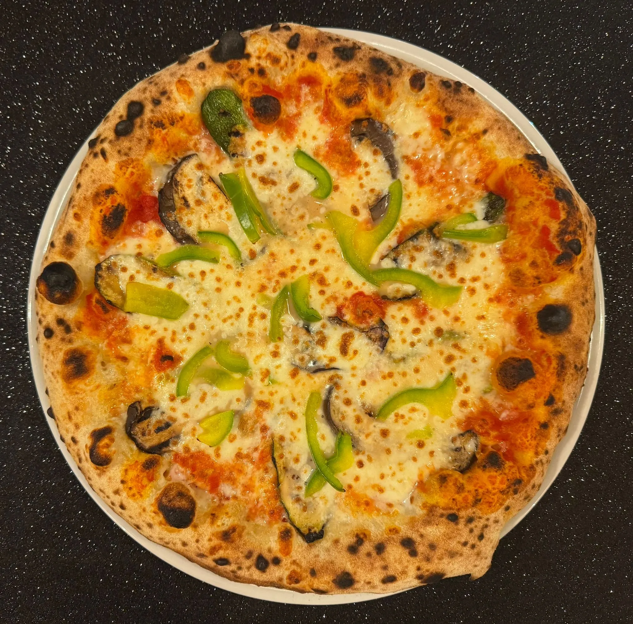 Pizza de Il Quartino con mozzarella, pomodoro, peperoni verdi e melanzane grigliate, cornicione bruciacchiato su piatto bianco